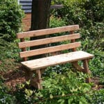 Cedar Backed Bench placed in garden environment, emphasizing natural golden finish and sturdy legs as reliable wood bench outdoor furniture