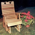 Cedar Royal Country Hearts Glider Chair in garden setting, showcasing honey-brown hue and lumbar support as a charming wood glider for porches.